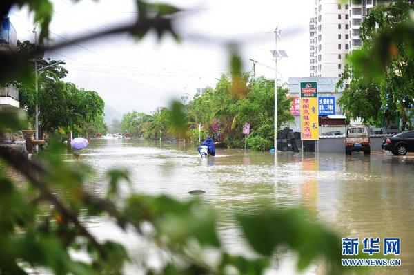 6月23日，在海南省三亞市，人們在積水路段涉水前行。今年第8號臺風“鯨魚”已于6月22日18時50分左右在海南省萬寧市沿海登陸，臺風給三亞帶來了強風降雨天氣，影響市民正常出行。新華社發（沙曉峰 攝）