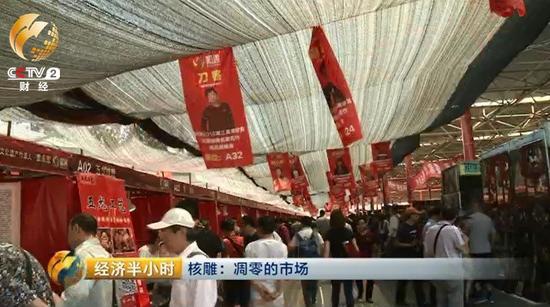 潘家園舊貨市場(chǎng)的這塊空地上，臨時(shí)支起了一些棚子和攤位，正在舉辦一個(gè)核雕展銷會(huì)。頂棚上方高高懸掛著前來(lái)參加展銷會(huì)的雕刻師的照片。
