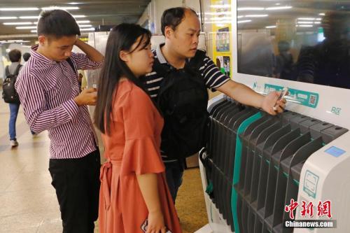 圖為沒(méi)帶雨傘的民眾在共享雨傘的貨架上掃碼借用。殷立勤 攝