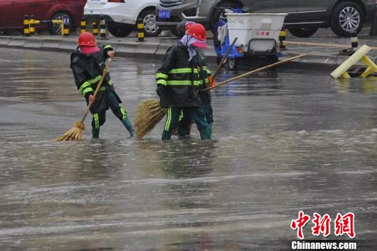 圖為環衛工人們冒雨清掃路面。　鄧建青 攝